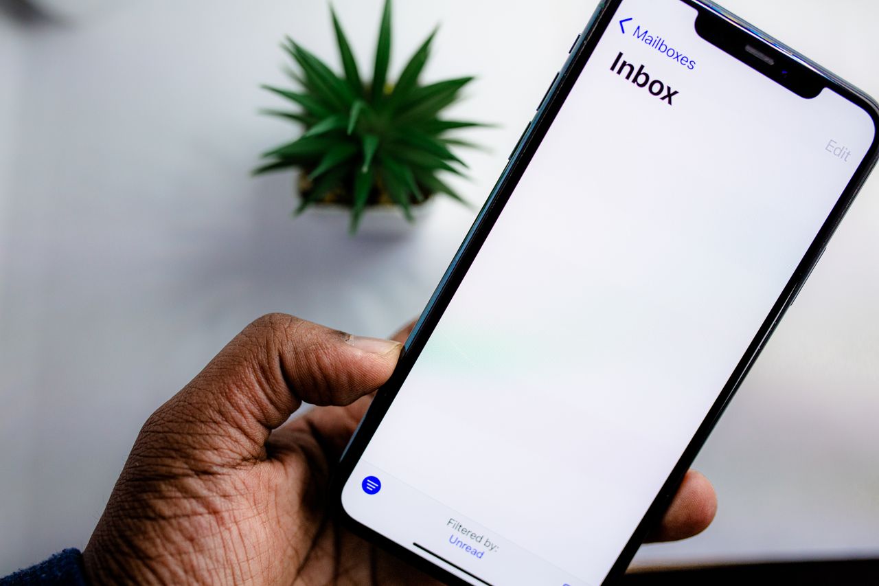 Vue rapprochée de l’écran d’un smartphone affichant la boîte de réception des e-mails, tenu par la main d’un adulte.